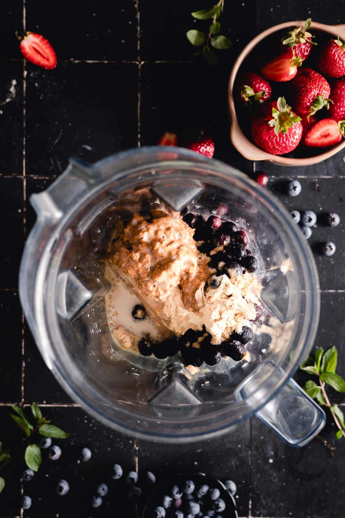 Frozen bananas, blueberries, protein powder, almond butter, and milk in a blender.