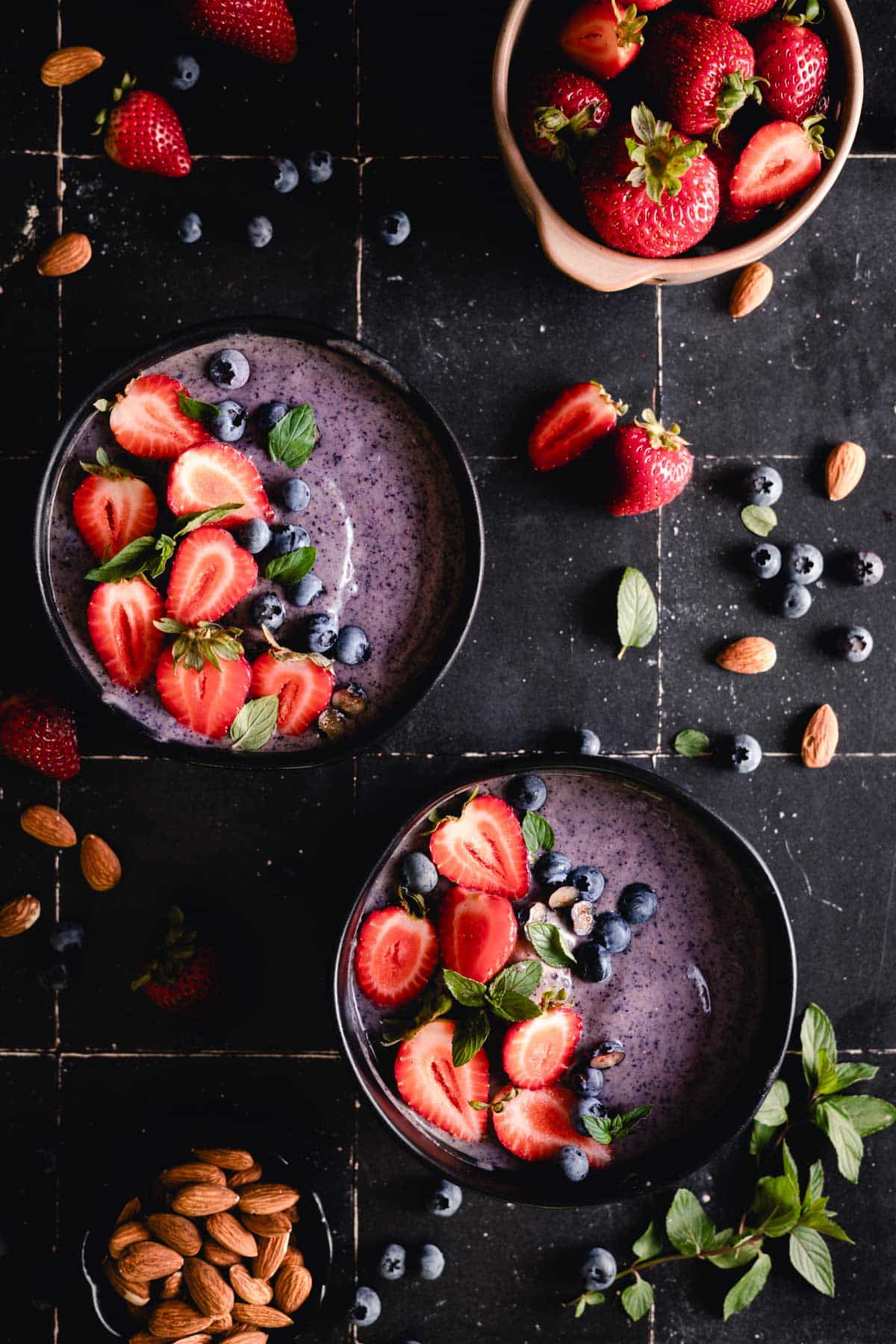 Purple blueberry smoothie bowls with fresh strawberries and blueberries on top.