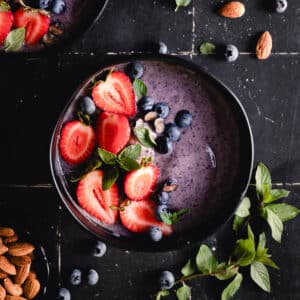 Purple blueberry smoothie bowls with fresh strawberries and blueberries on top.