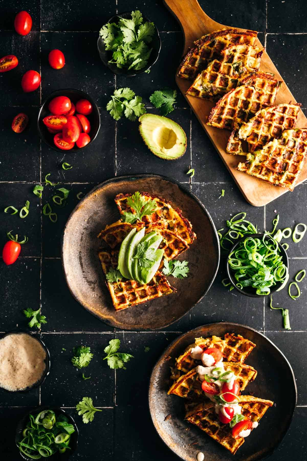 Waffle slices with avocaco, cilantro, green onions and tomatoes on top.