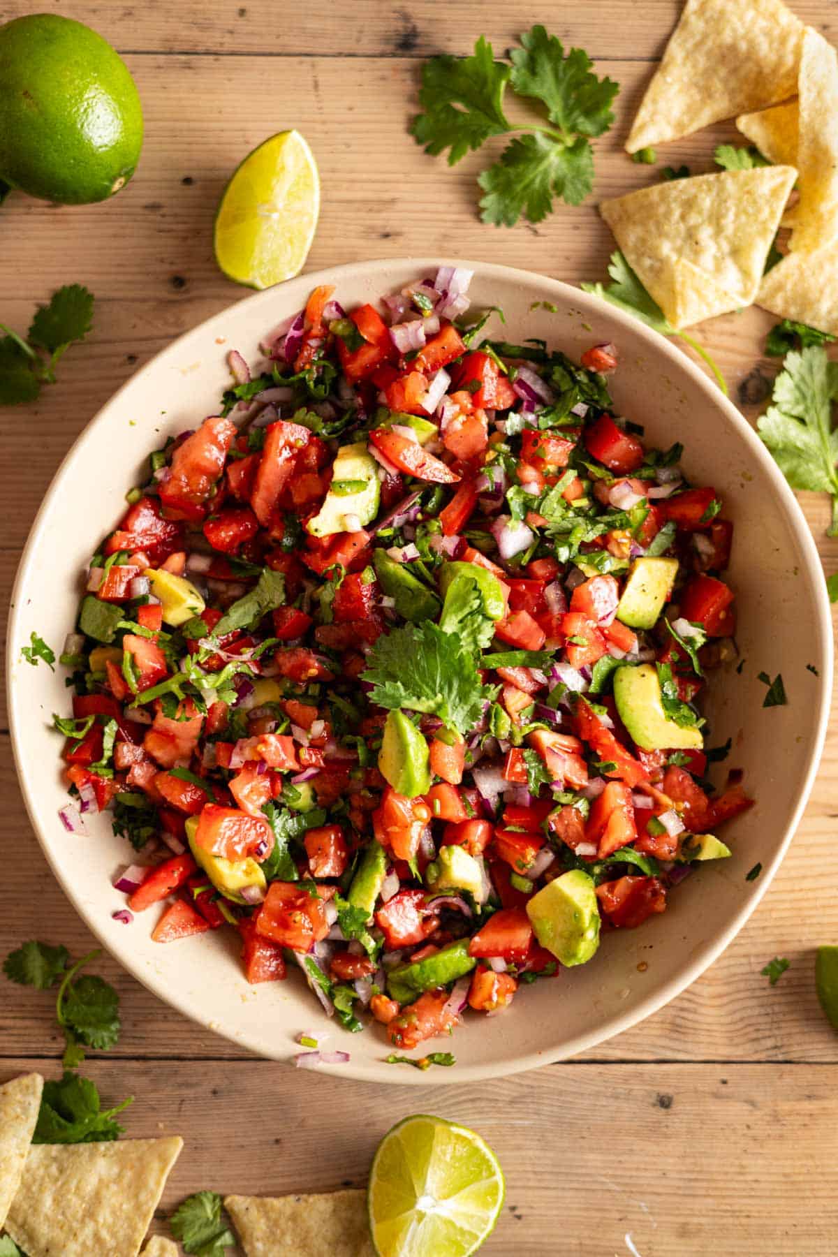 Homemade avocado pico in a shallow cream bowl with lime wedges and cilantro sprigs next to it.