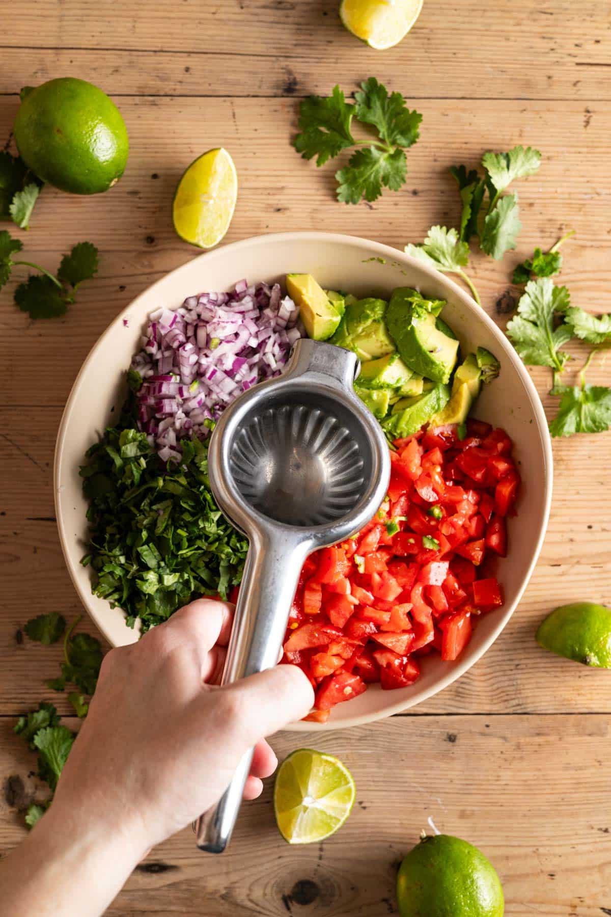 Fresh lime juice being squeezed into a bowl filled with chopped fresh veggies.