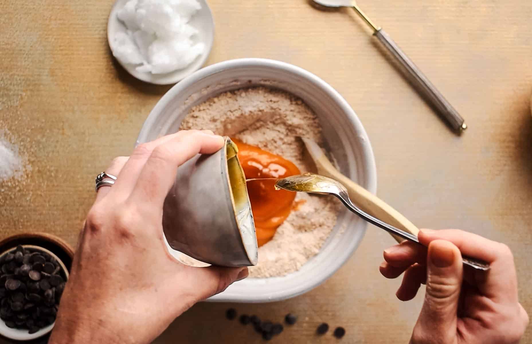 Adding wet ingredients into the large mixing bowl for homemade cookies.