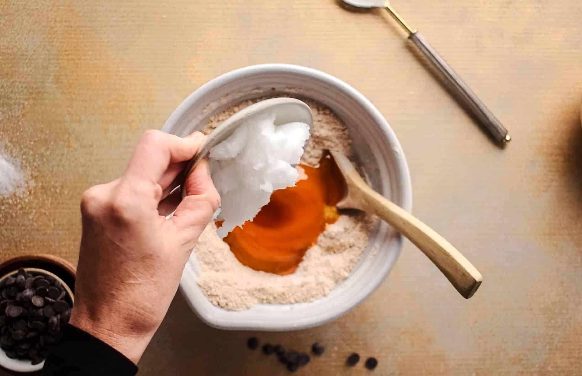 Adding wet ingredients into the large mixing bowl for homemade cookies.