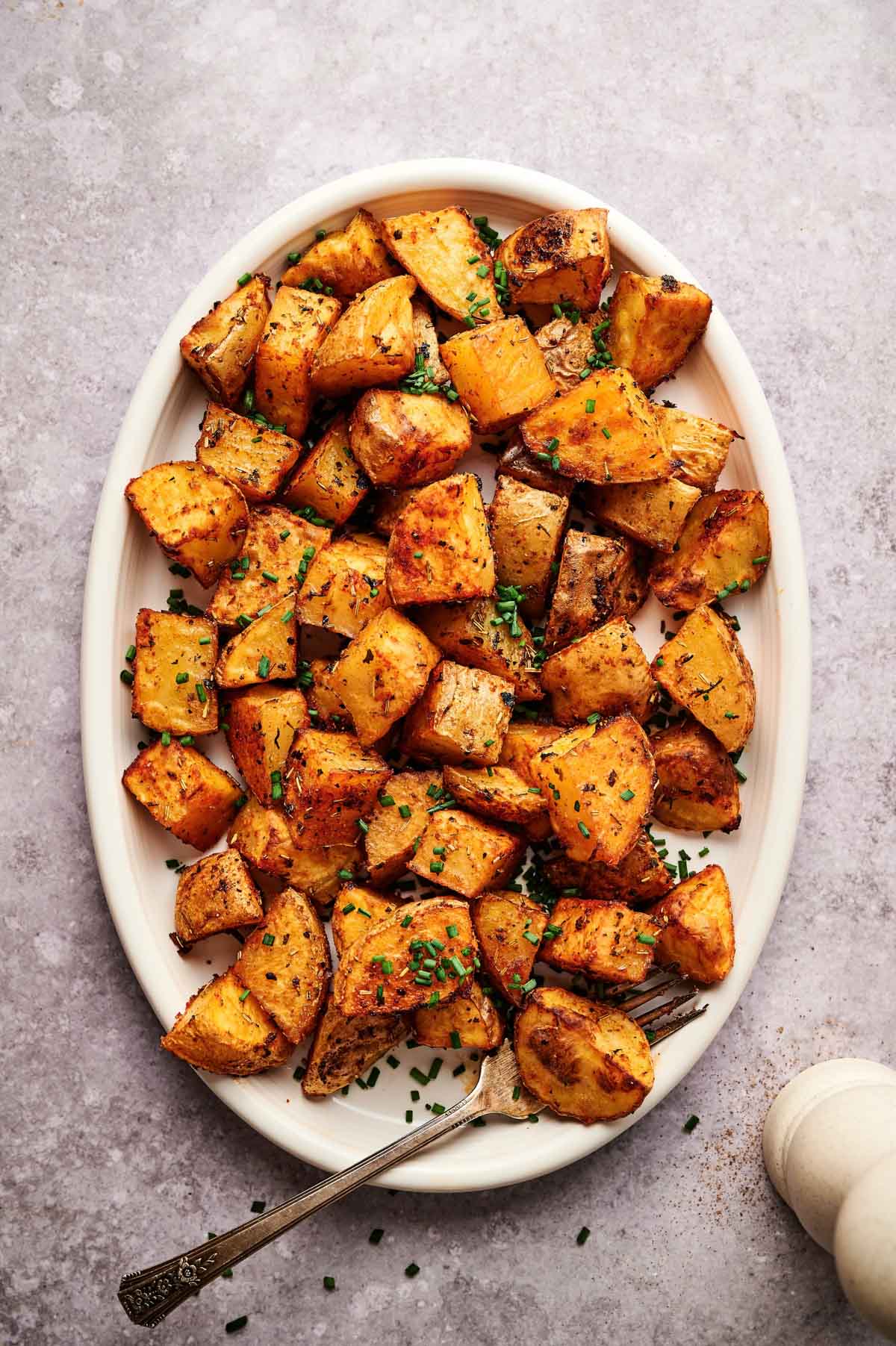 White plate of oven oven baked home fries with fresh chopped chives on top.