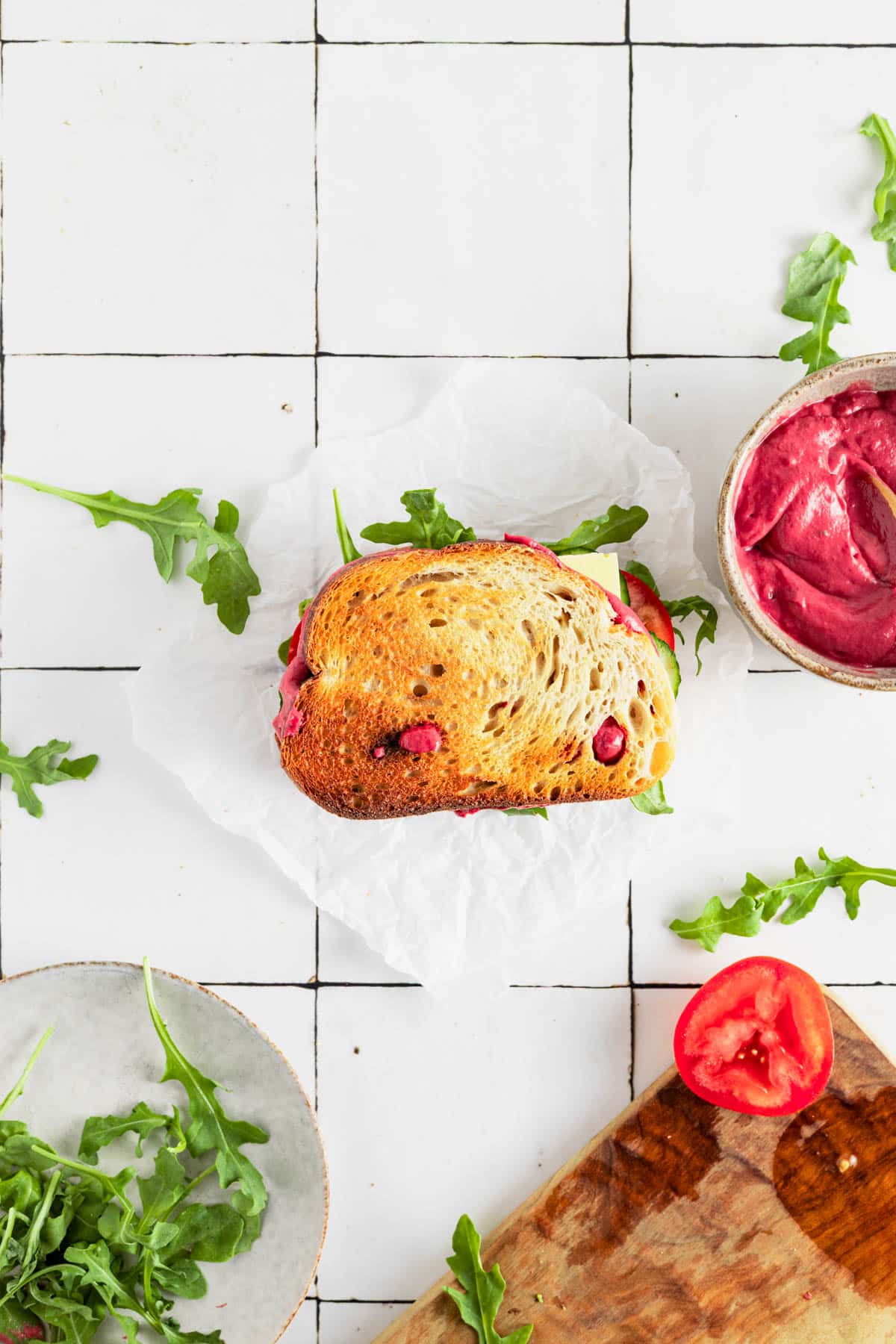 Assembled beet hummus sandwich with fresh arugula on the counter.