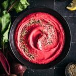 Fresh beet hummus in a large black bowl on a black tiled counter.