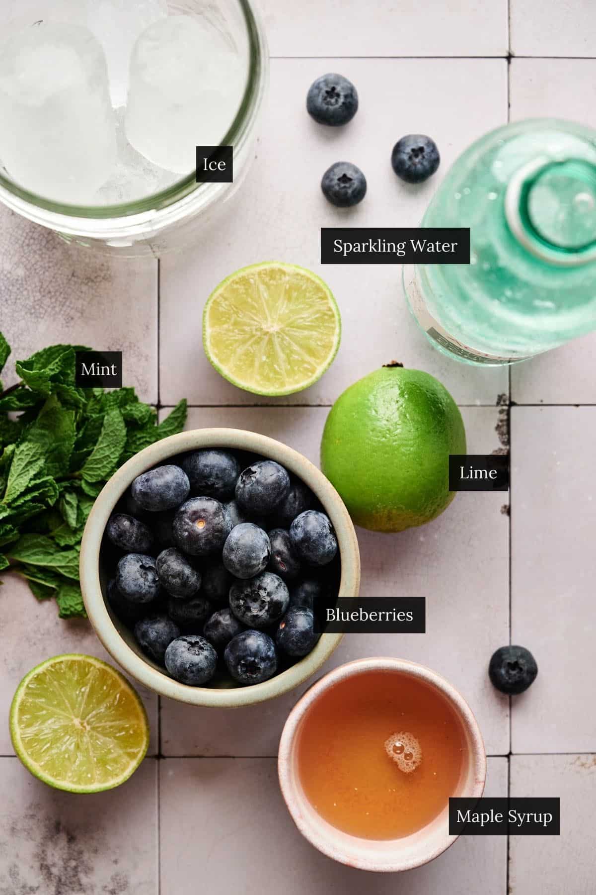 Ingredients for blueberry mocktail on a white tile table with each ingredient labeled.