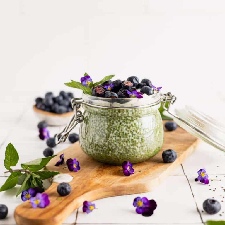 Fresh blueberries on top of a green tea chia seed pudding with fresh mint and purple edible flowers.