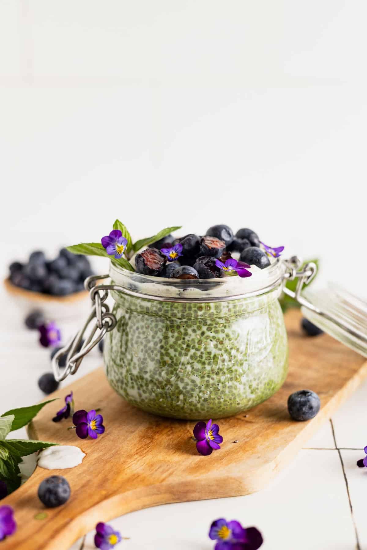 Fresh blueberries on top of a green tea chia seed pudding with fresh mint and purple edible flowers.