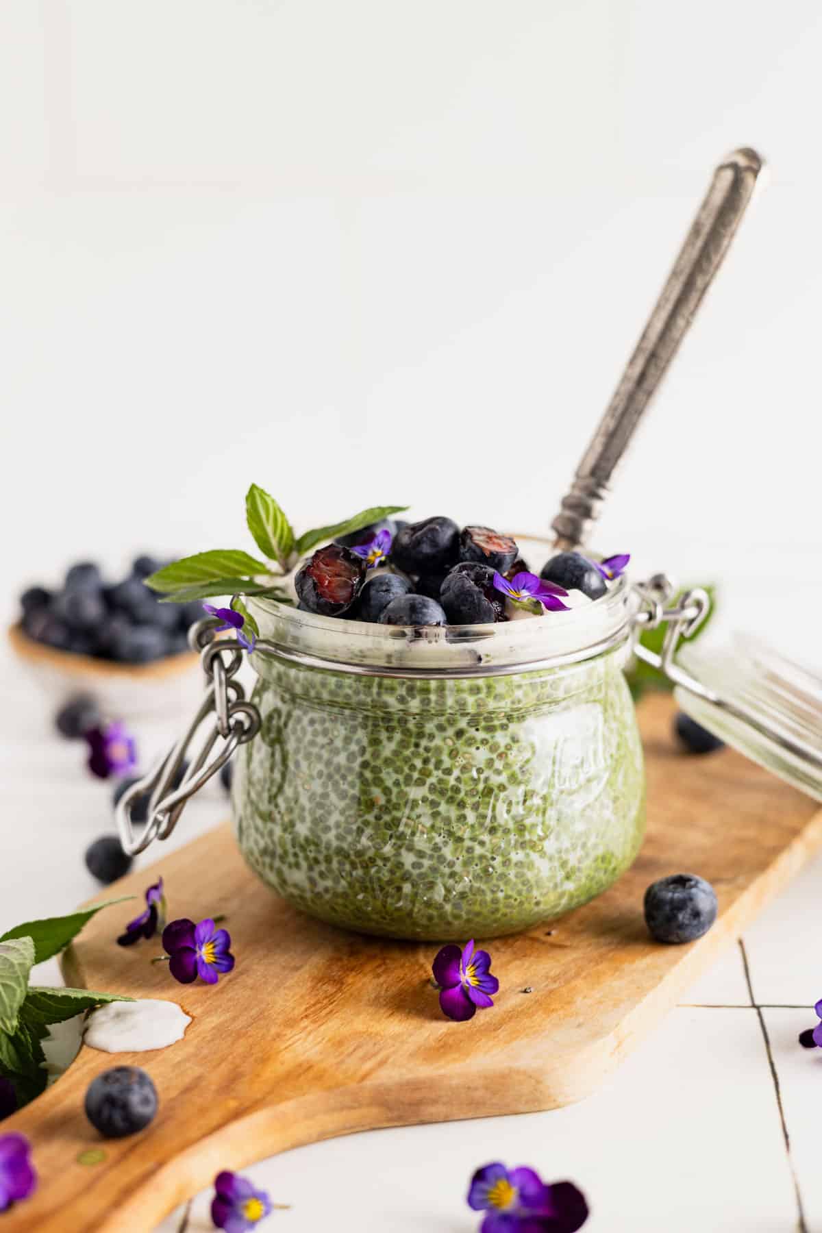 Fresh blueberries on top of a green tea chia seed pudding with fresh mint and purple edible flowers.
