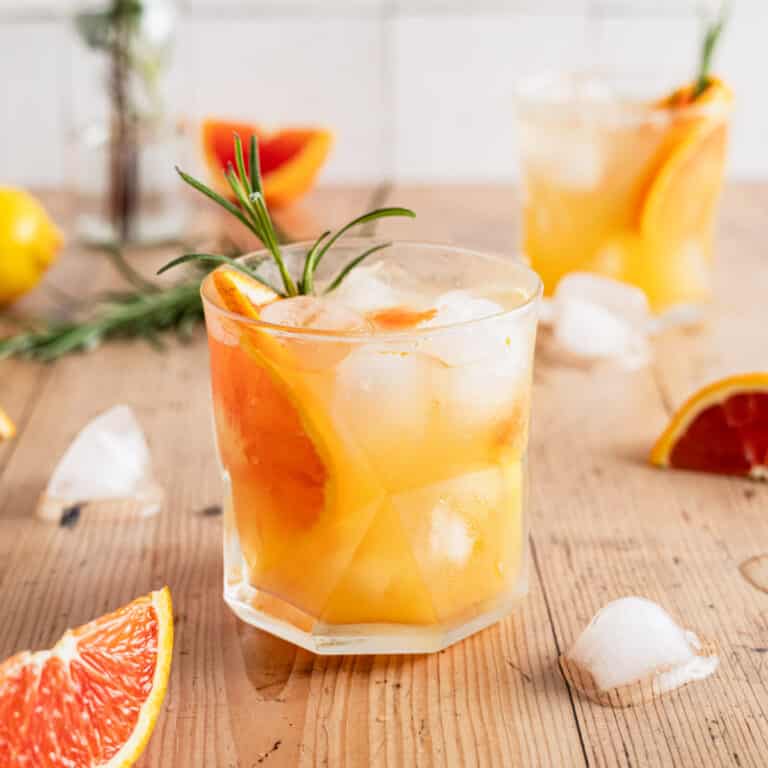 Homemade orange spritz with fresh orange slice and rosemary in glass cup.