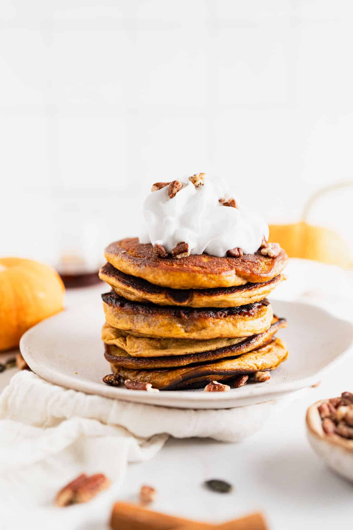 Protein pumpkin spice pancakes stacked with whipped cream and pecans on top.