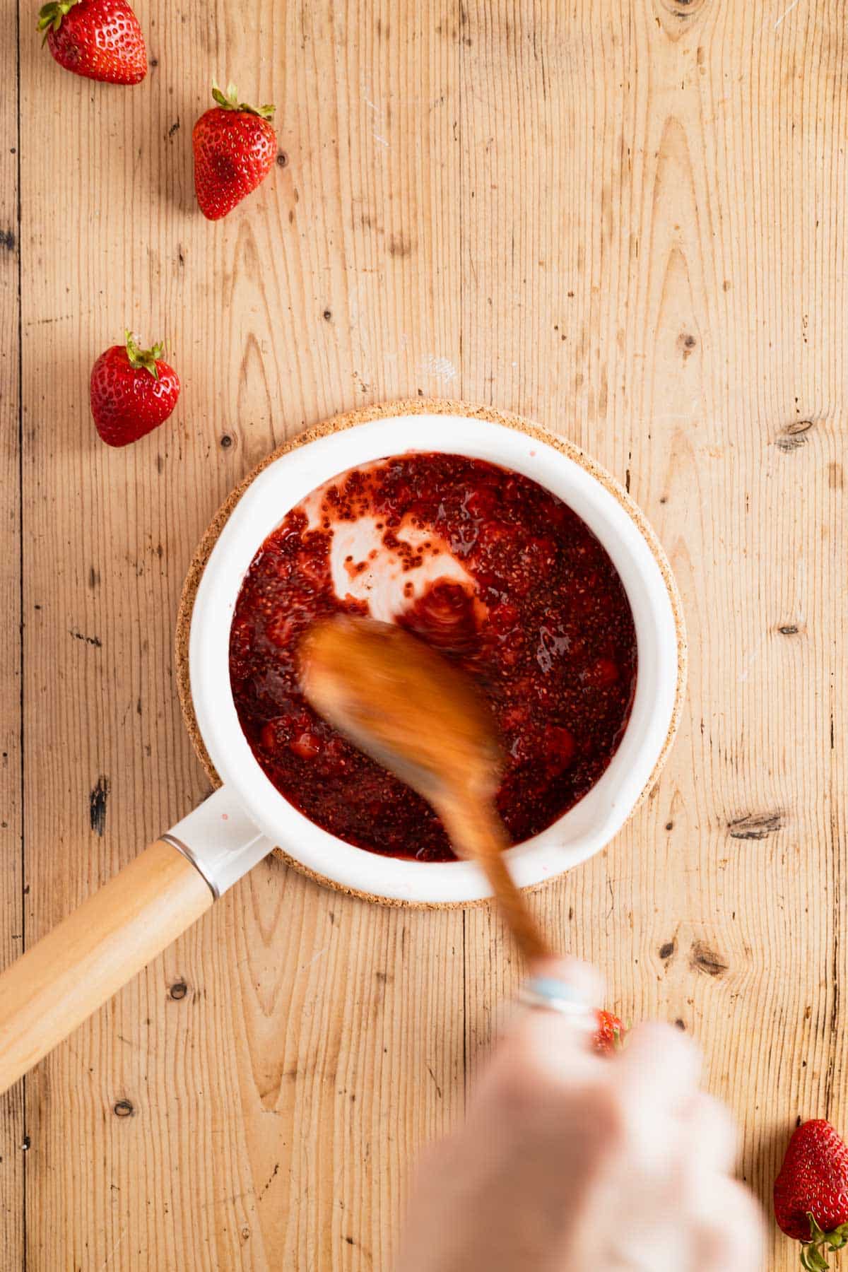 Stirring mashed strawberries in a saucepan.