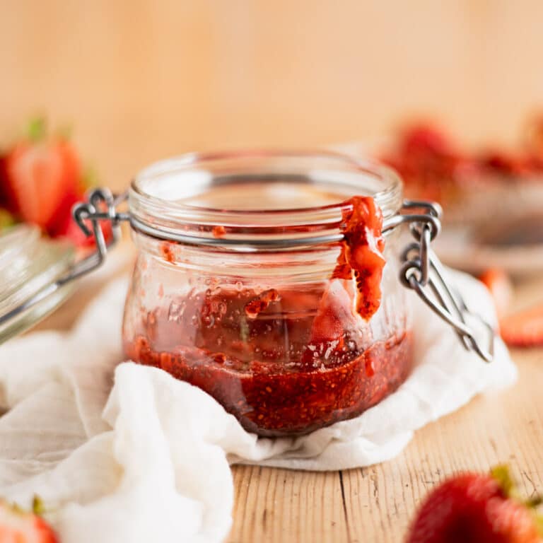 Chia seed strawberry jam in a glass jar on a white linen napkin.