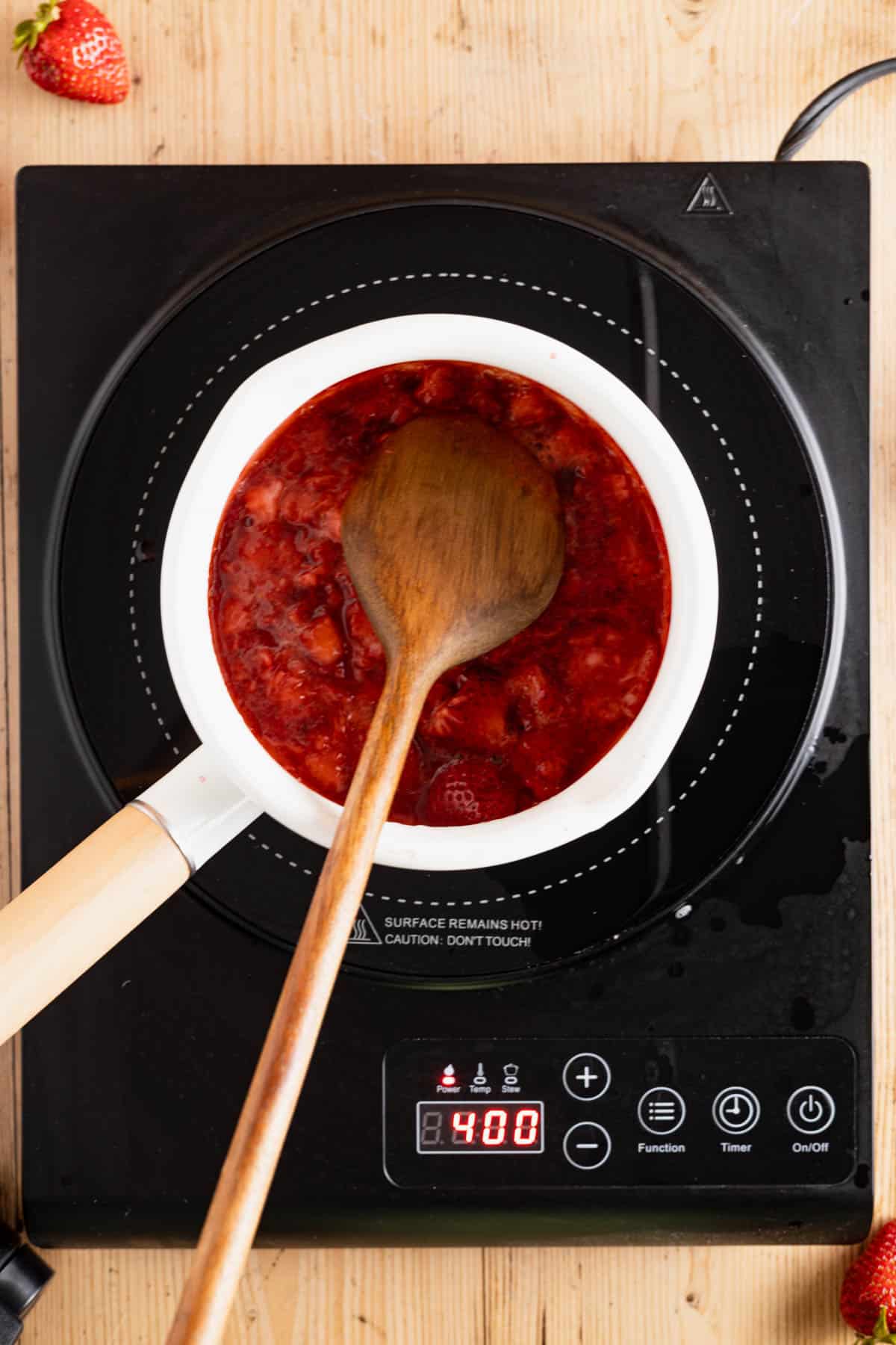 Stirring mashed strawberries in a saucepan.