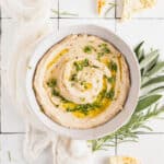 Homemade white bean dip in a white bowl with olive oil drizzled on top and fresh herbs.