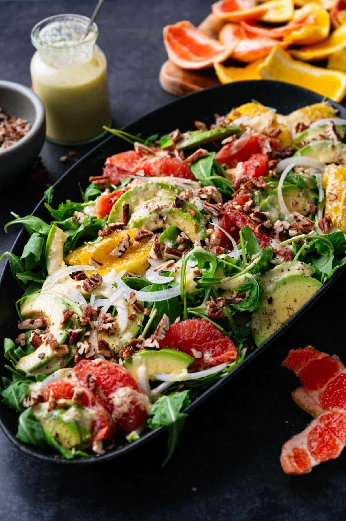 Close up of vibrant green salad with avocado and pink and orange oranges.