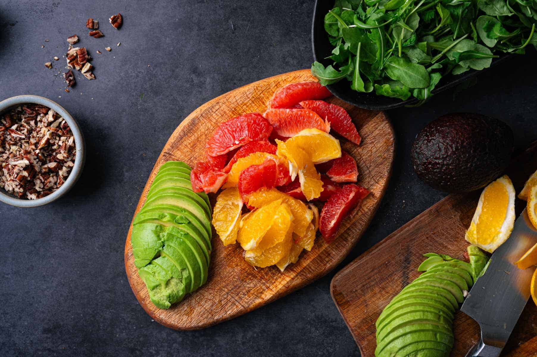 Oranges and avocado sliced on a wooden cutting board.