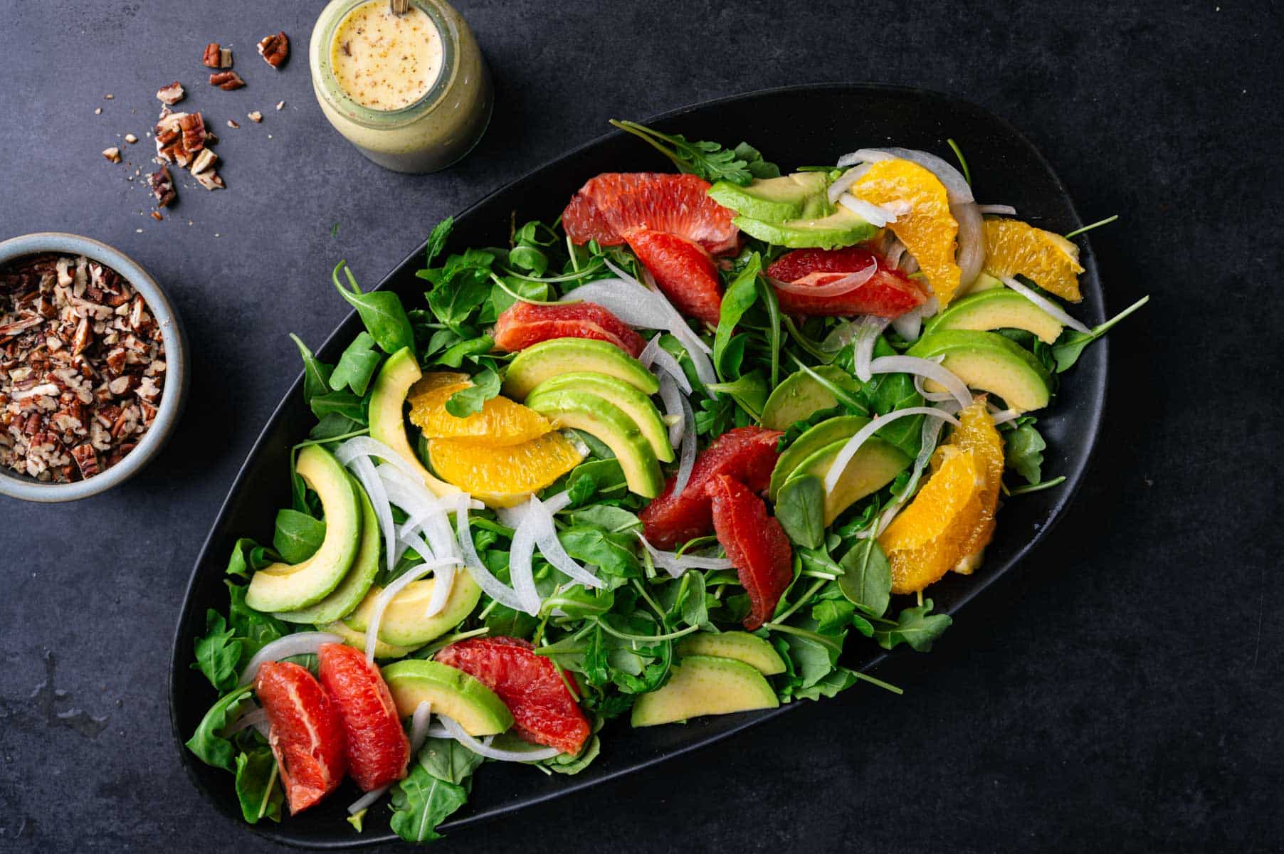 Oranges, avocado, onion, and greens spread out on a platter.