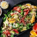 Flavorful arugula and orange salad on a large black serving platter.