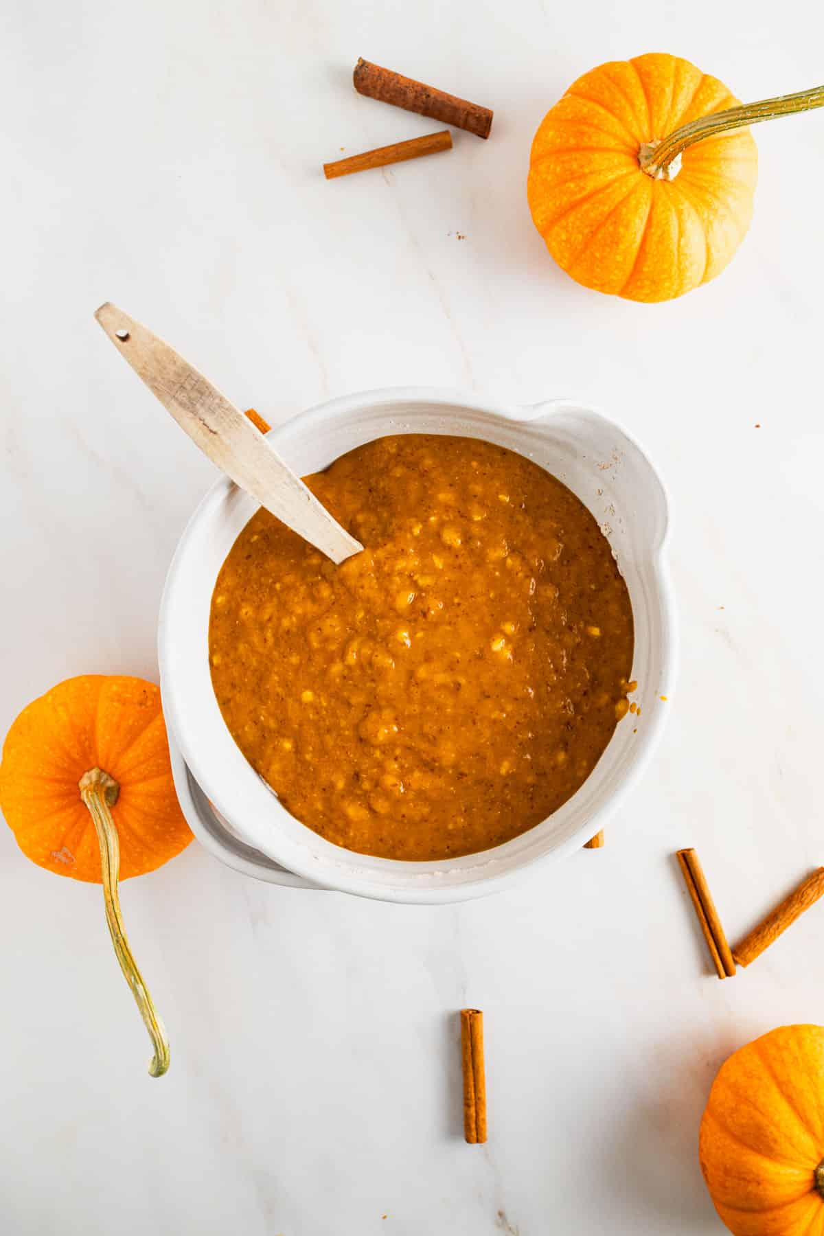 Wet ingredients for pumpkin muffins with banana added to a mixing bowl with dry ingredients.