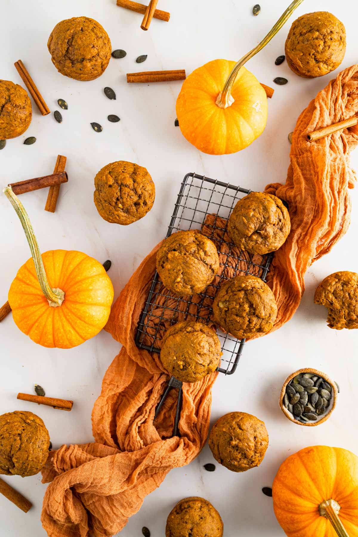 Fluffy banana pumpkin muffins on a small cooking rack with an orange gauze napkin underneath.