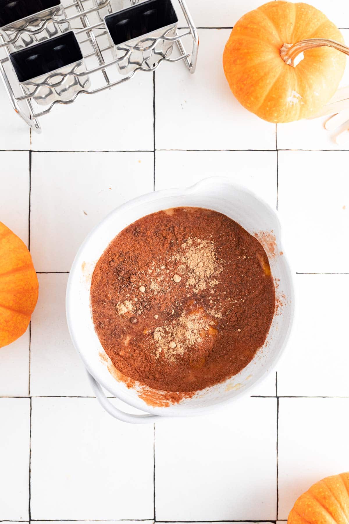 Adding all the ingredients for pumpkin popsicles to a mixing bowl.