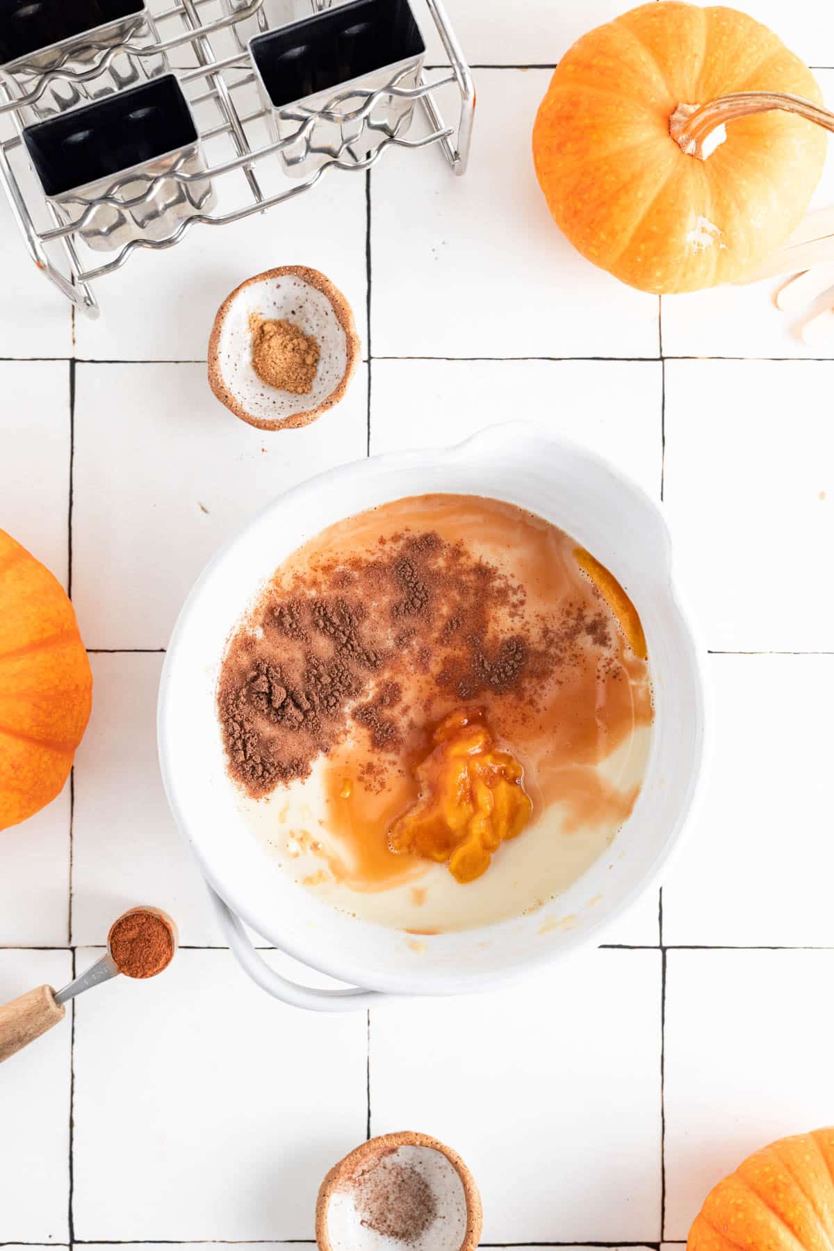 Adding all the ingredients for pumpkin popsicles to a mixing bowl.