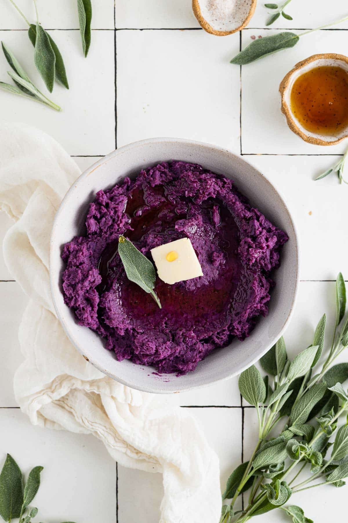 Vegan mashed sweet potatoes on white tile counter with fresh sage and butter.