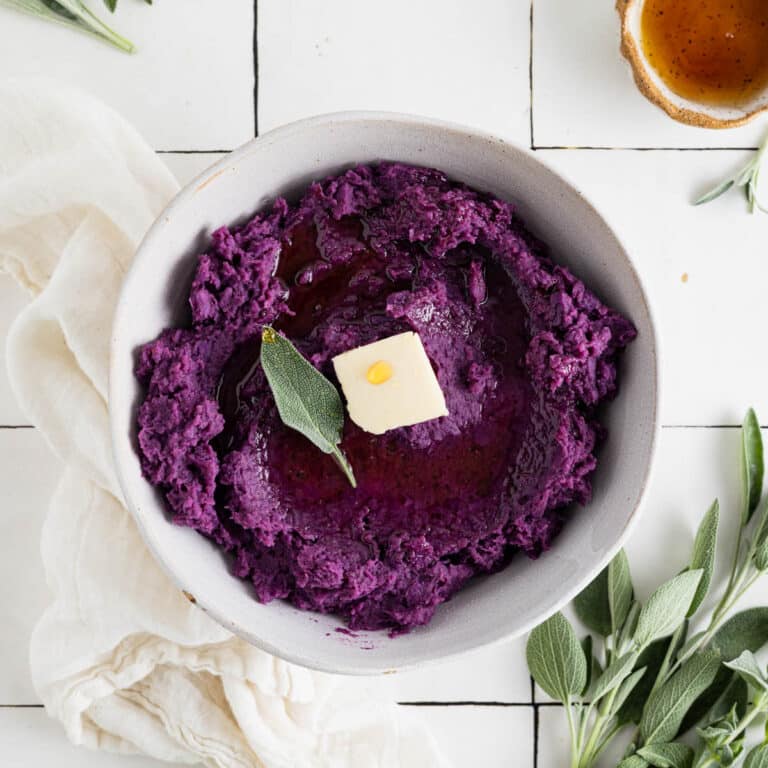 Vegan mashed sweet potatoes on white tile counter with fresh sage and butter.