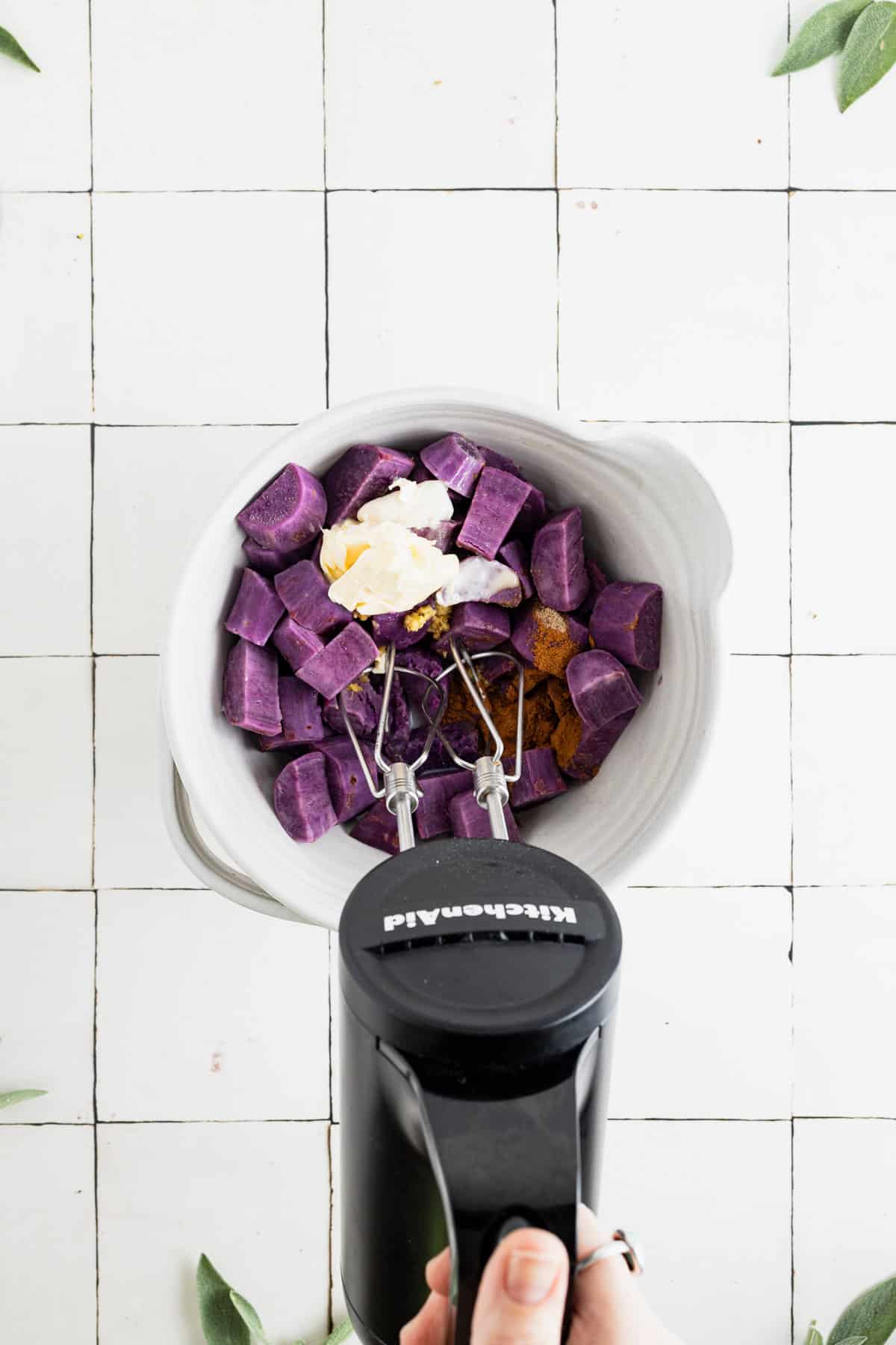 Using a hand mixer to whip and mix the sweet potato casserole ingredients.