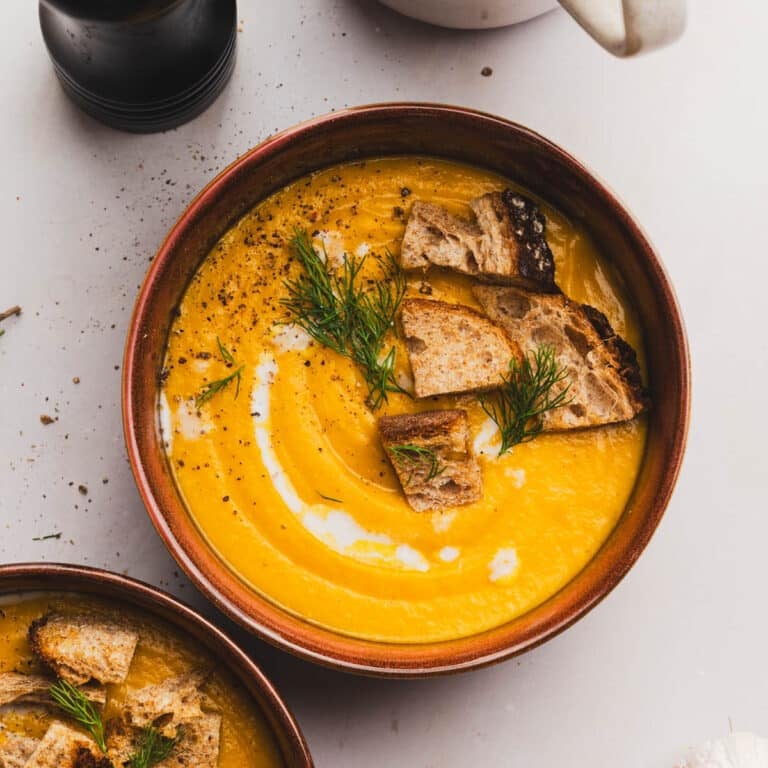 Bowl of deep yellow-orange soup with crispy bread and fresh herbs on top.