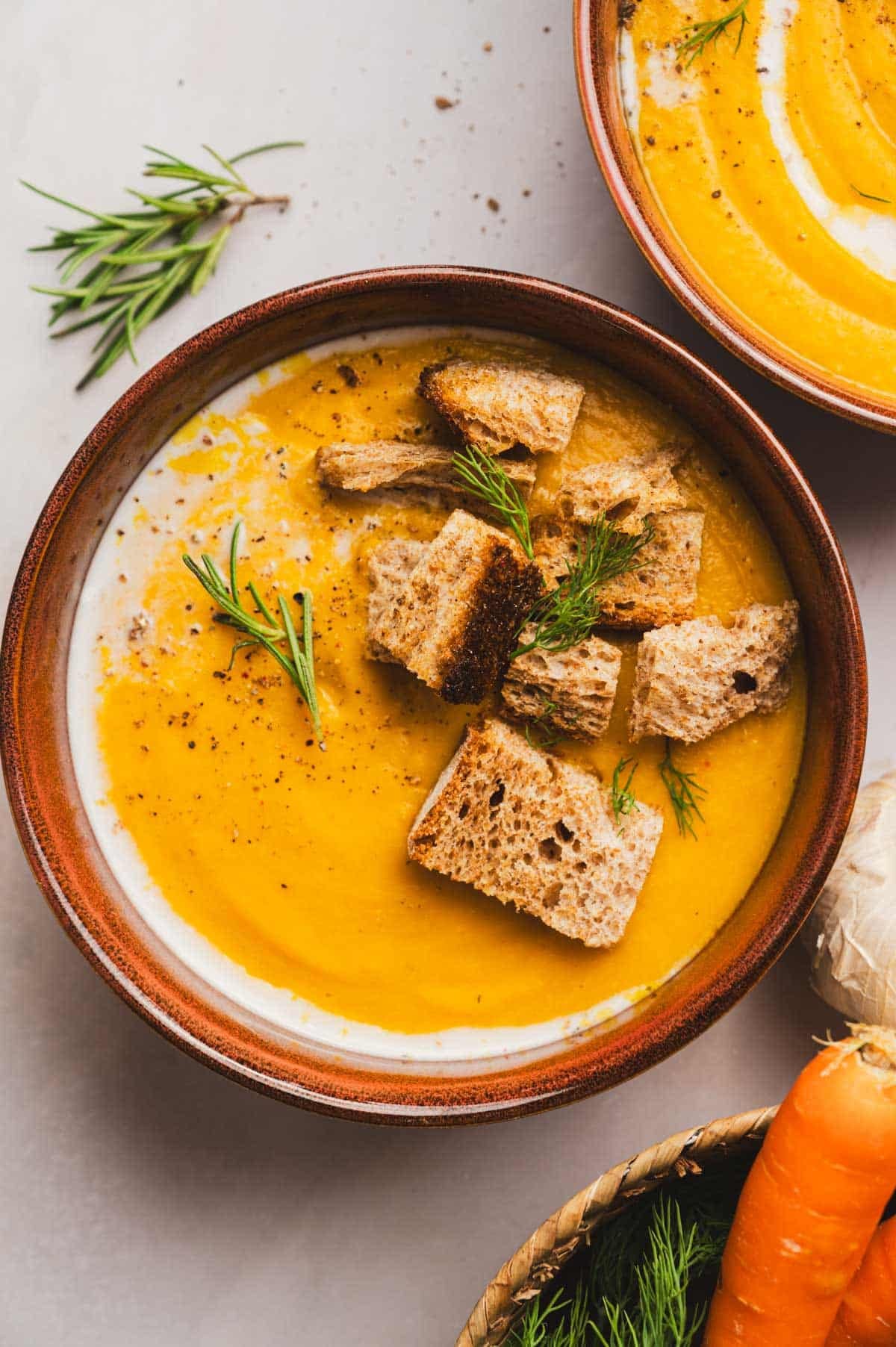 Bowl of deep yellow-orange soup with crispy bread and fresh herbs on top.