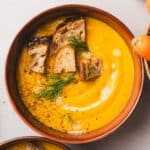 Bowl of deep yellow-orange soup with crispy bread and fresh herbs on top.