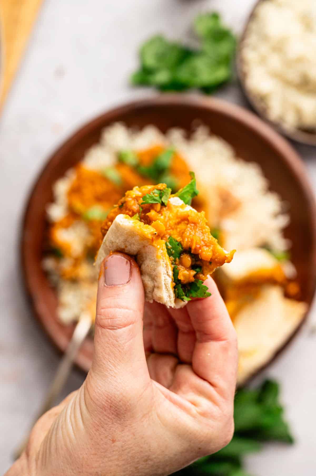Woman picking up a piece of pita bread filled with tikka masala and herbs.