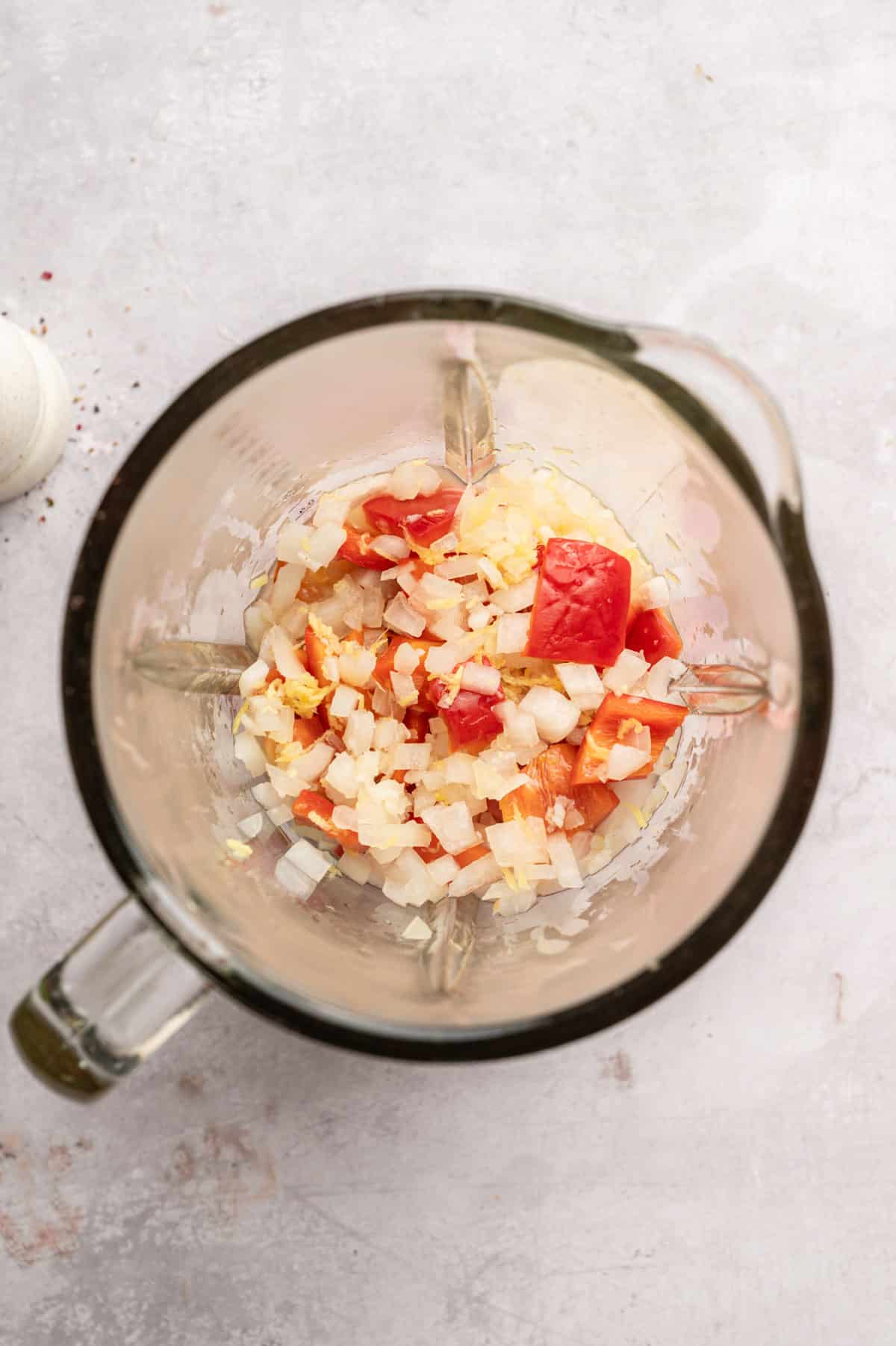 Adding sautéed onion, garlic, ginger, and red bell pepper to a blender.