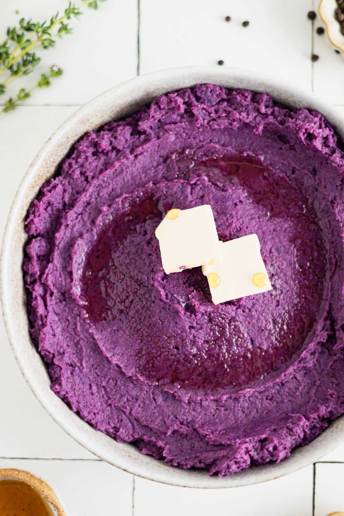 Whipped vegan sweet potatoes in a shallow bowl on a tile counter with vegan butter and fresh thyme.