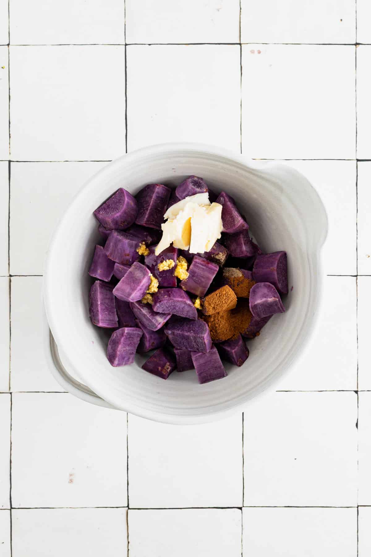 Cooked sweet potato chunks in a large white mixing bowl with spices.