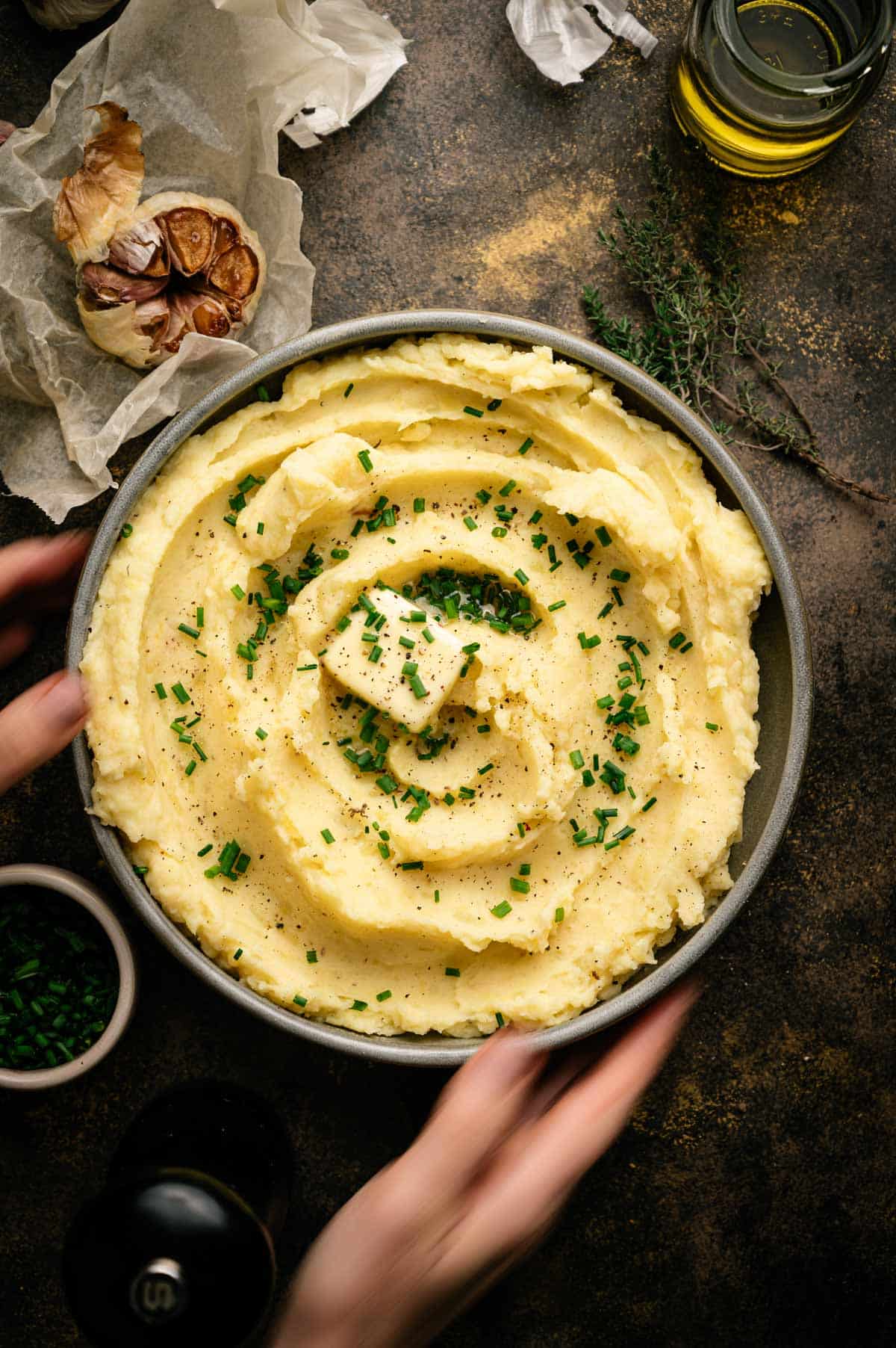 Woman reaching for large shallow bowl filled with mashed potatoes.