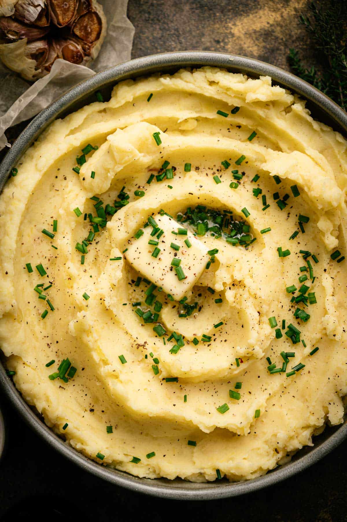 Close up of homemade vegan mashed potatoes on a shallow bowl with a square of melting vegan butter and chives on top.