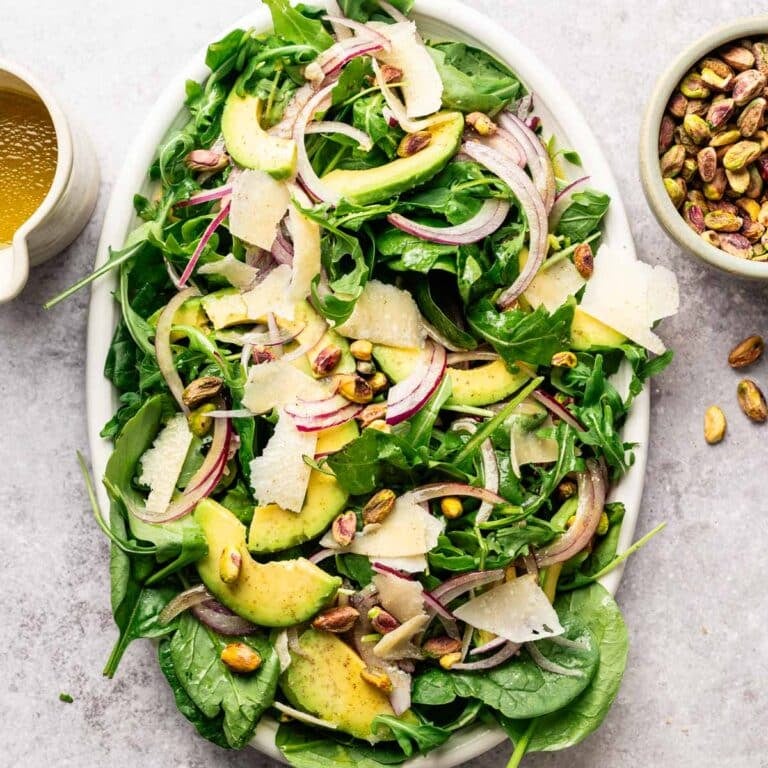 Arugula and spinach salad with sliced avocado, onion, pistachios, and shaved vegan Parmesan.