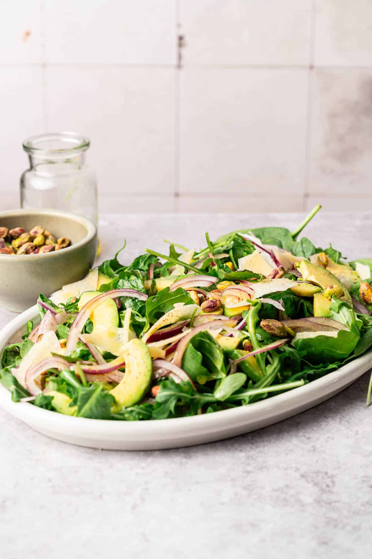 Arugula and spinach salad with sliced avocado, onion, pistachios, and shaved vegan Parmesan.