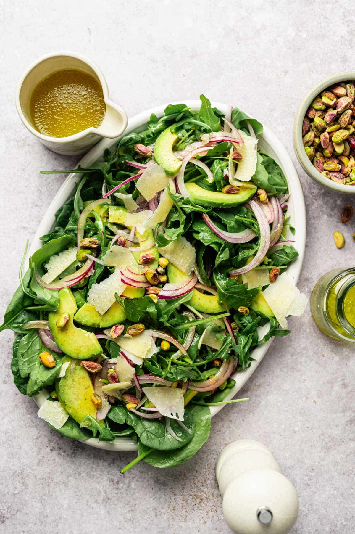 Spinach and arugula salad on a large white oval platter with sliced avocado and onion.