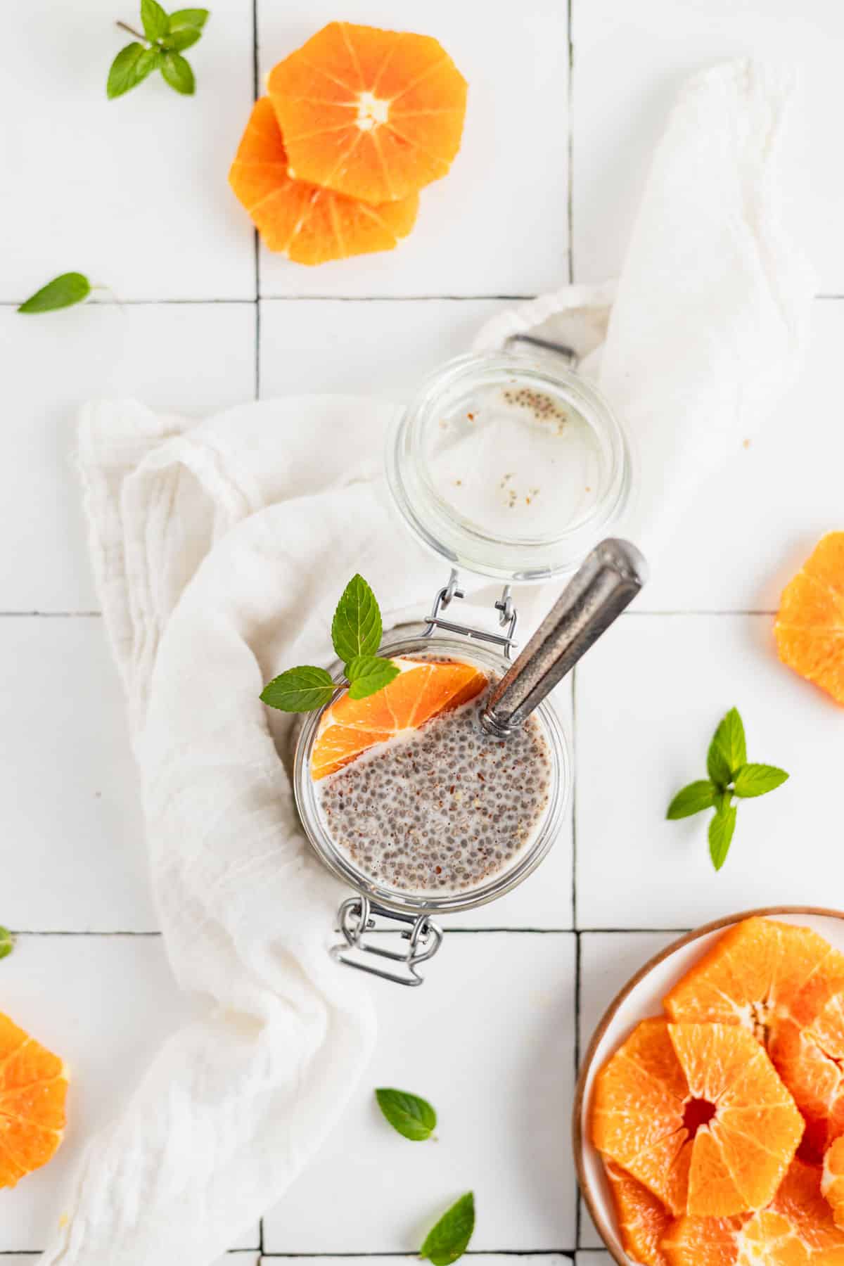 Top down view of ground flax and chia seed pudding in a clear glass jar with orange slices and fresh mint sprigs.