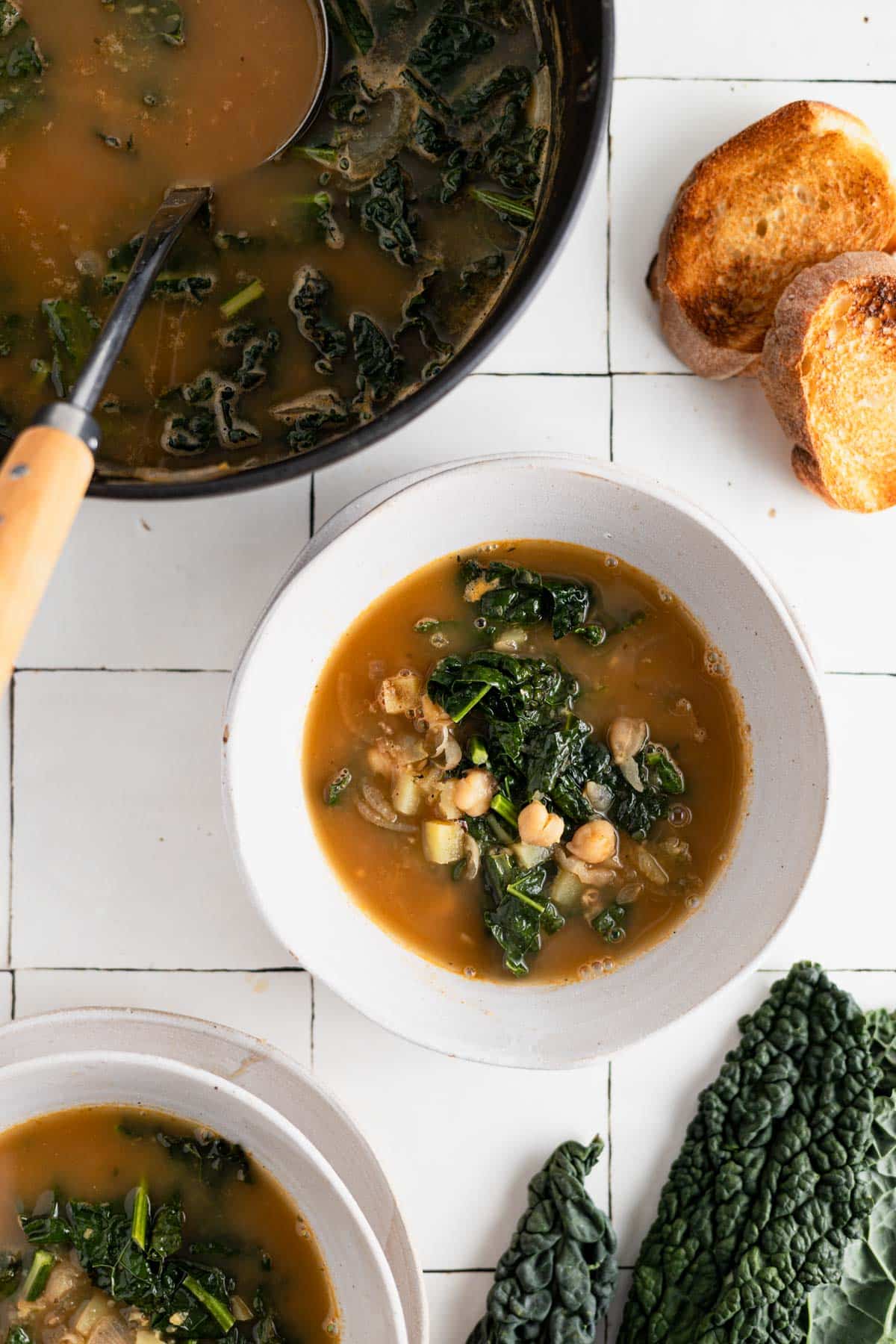 Garbanzo bean kale soup scooped into a white bowl with the black Dutch oven next to it.