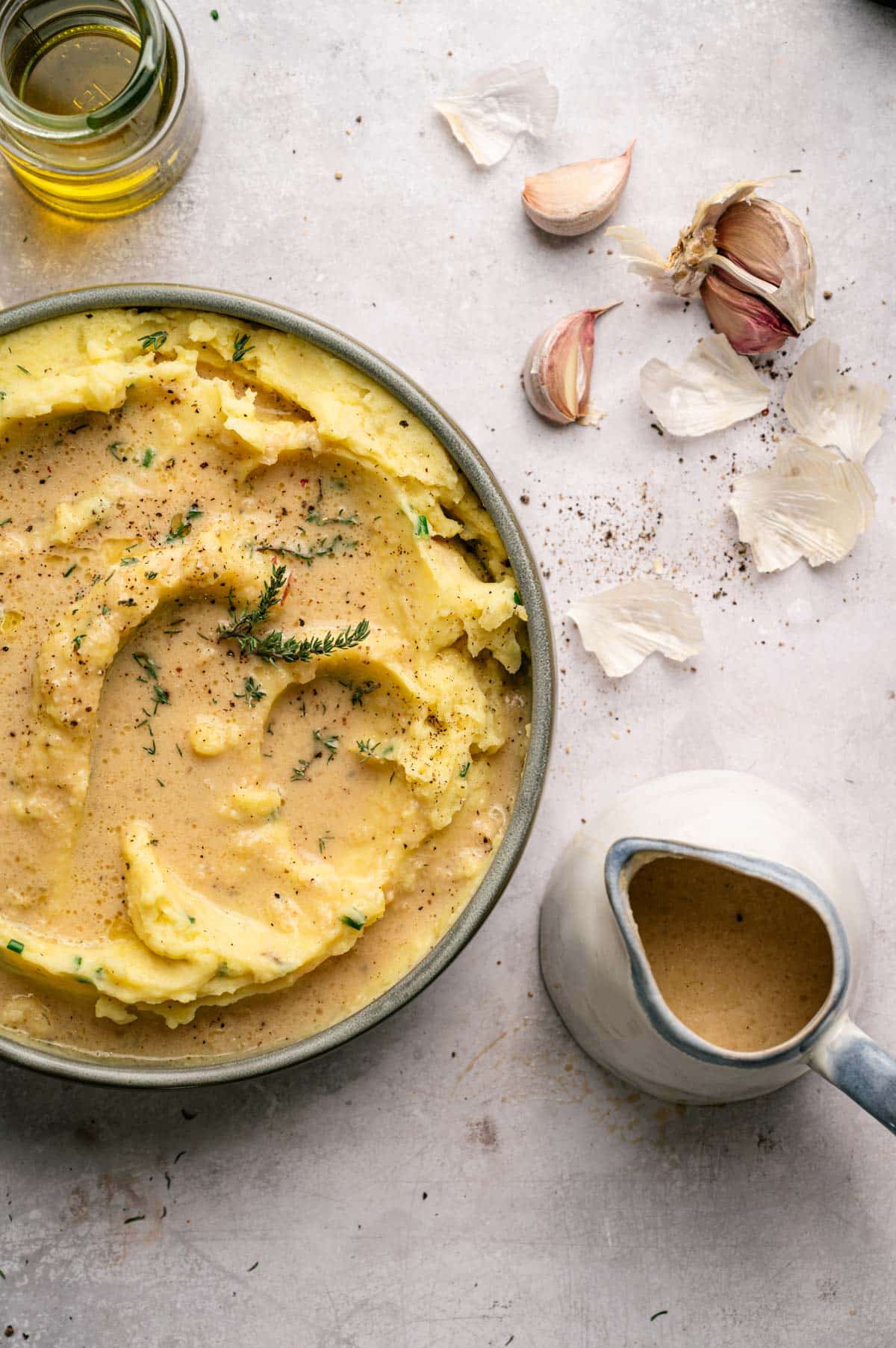 Mashed potatoes in a shallow bowl covered in vegan gravy and fresh herbs.