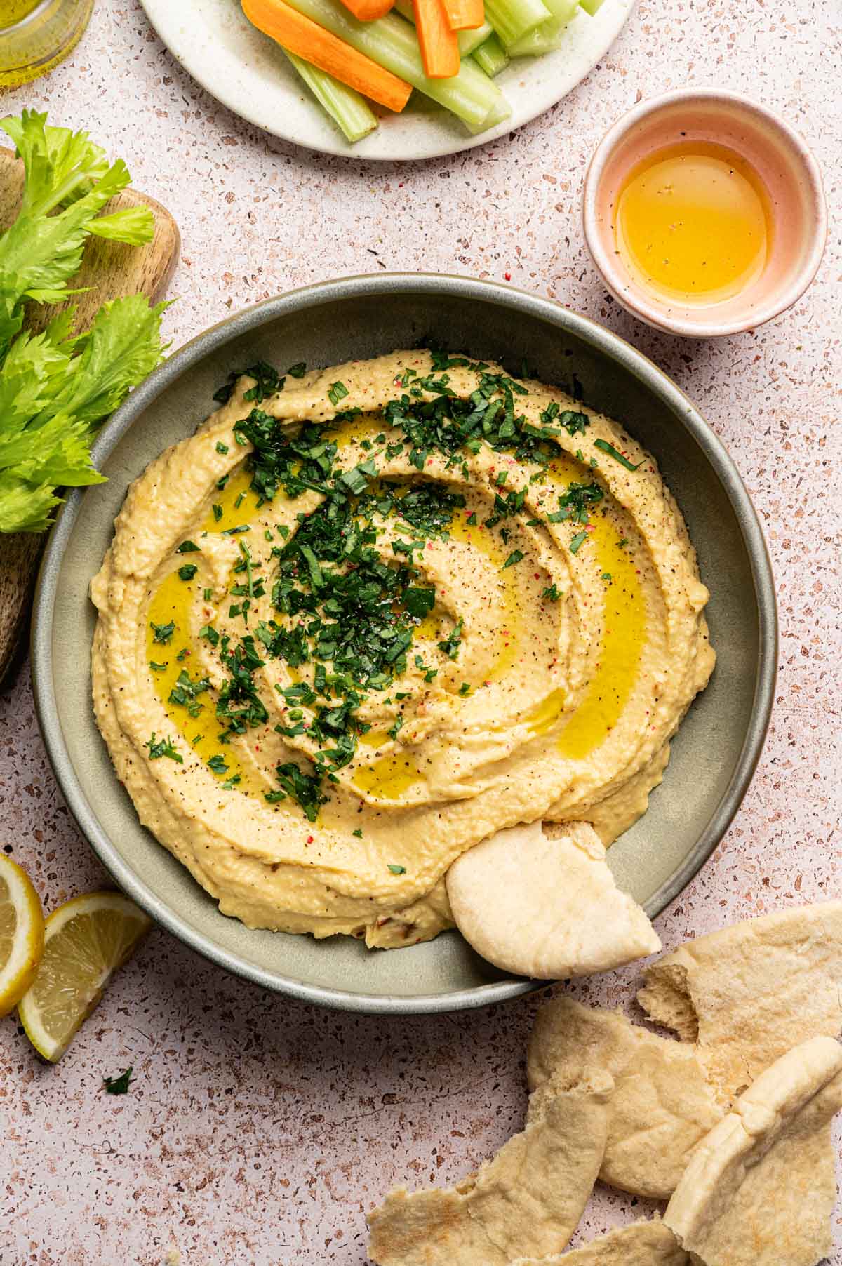 Roasted garlic hummus in a shallow green plate with olive oil and fresh herbs on top and pita bread.