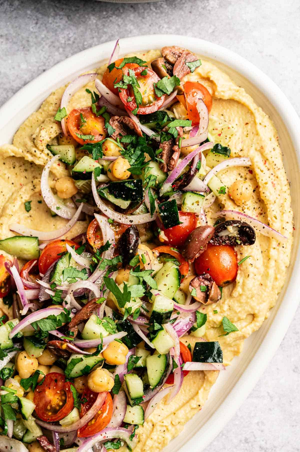 Close up of loaded hummus dip on an oval white platter.