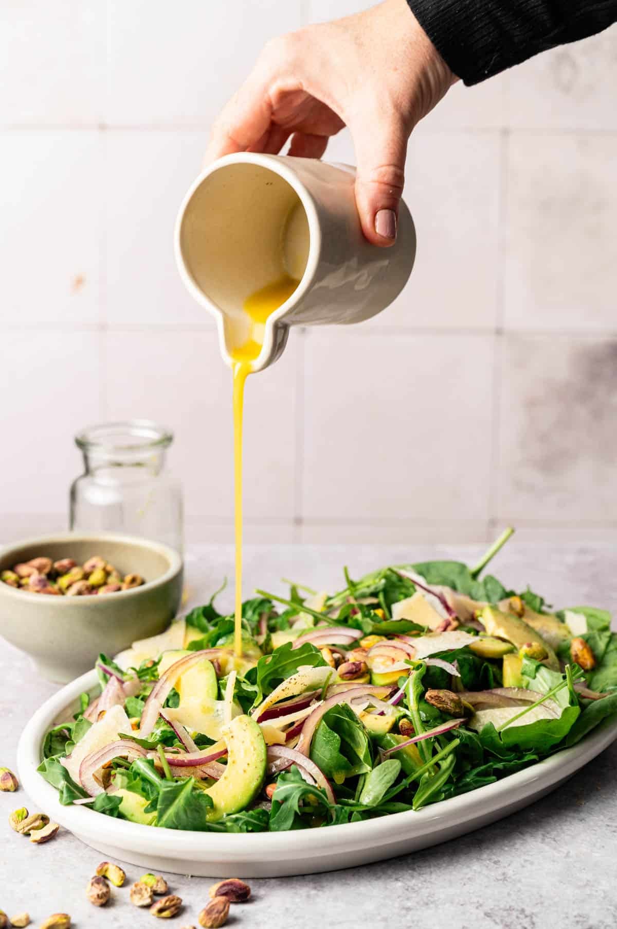 Dijon and maple salad dressing being poured over a green salad.